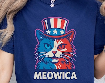 May include: Navy blue t-shirt featuring a patriotic cat design. The cat is split into red and blue halves, wearing an Uncle Sam hat with stars. The word "MEOWICA" is printed below the cat in white letters.