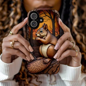 May include: A phone case with a brown squirrel sitting on a tree branch. The background is a sunset with trees and a yellow sky. The case has a camera lens cutout.