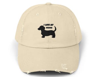 Puede incluir: Gorra de béisbol beige desgastada con visera curva. La gorra presenta el texto "I LOVE MY WEINER" sobre una silueta negra de perro salchicha. La gorra tiene un aspecto vintage y desgastado con bordes deshilachados.