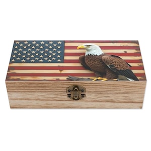 May include: Wooden box with a distressed American flag design on the lid. A detailed sculpture of a bald eagle is perched on the box. The box has a metal clasp closure and a natural wood grain finish.