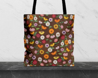 May include: A brown tote bag with a colorful floral pattern. The design features various flowers in shades of yellow, orange, pink, and white, set against a brown background. The bag has black handles.