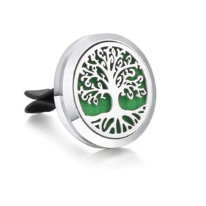 May include: A silver car air vent diffuser with a tree of life design. The tree is white, set against a green background. The diffuser has a black clip for attachment.