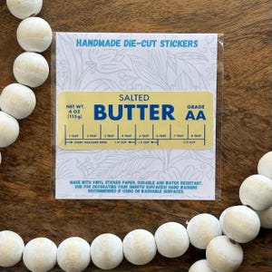 May include: A die-cut sticker with the words "SALTED BUTTER" in blue on a yellow background. The sticker includes a measurement guide and states the net weight as 4 oz (113g). The sticker is made of vinyl and is water resistant.
