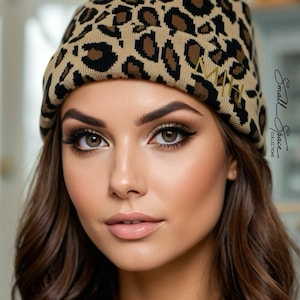 May include: A knit beanie featuring a tan and black leopard print pattern. The cuff of the beanie displays the gold embroidered letters MH. The text Small Space COLLECTIONS is visible on the right side of the image in a black script font.