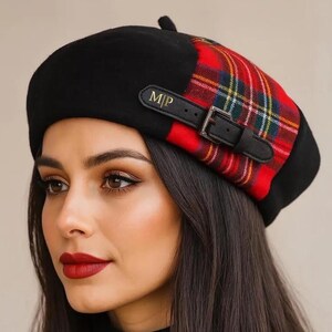 May include: A black beret featuring a red, green, and yellow tartan pattern on one side. A black leather-look strap with a silver buckle and the gold embossed letters M|P is attached to the side. The text Small Space COLLECTIONS is visible.
