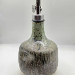 May include: A set of three ceramic mugs with a speckled, matte finish. The mugs are in shades of cream, light gray, and dark gray. Each mug has a simple, minimalist design and a rounded handle.