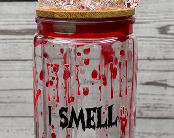 May include: A clear glass jar with a red rim and blood-like splatters. The jar has the text "I SMELL CHILDREN" in black. The lid is topped with red and clear decorative crystals and a clear straw.