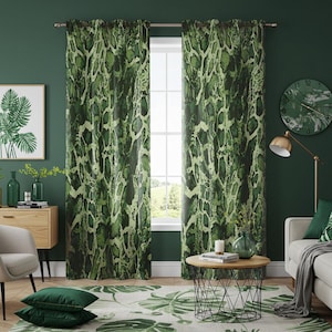 Puede incluir: Cortinas con estampado de serpiente verde y blanco colgadas frente a una ventana. Las cortinas son el punto focal de una habitación con una pared verde, un mueble de madera y una mesa de centro redonda. Una alfombra con estampado de hojas verdes y blancas está en el suelo.