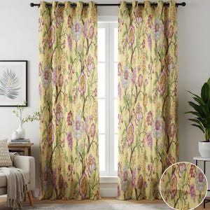 Op de afbeelding: Twee gele gordijnen met bloemenprint, met een stangenzak en ogen. De gordijnen hebben een herhalend patroon van grote bloemen in roze, paars en wit, met groene bladeren en bruine takken. Ze hangen voor een raam.