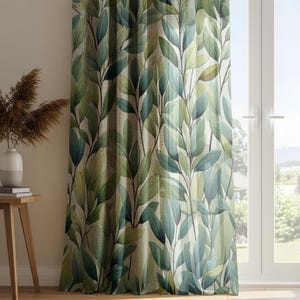 Könnte beinhalten: Ein Vorhang mit einem grünen und blauen Blättermuster. Der Vorhang hängt vor einem Fenster. Links vom Vorhang befindet sich ein kleiner Holztisch mit einer weißen Vase und getrockneten Pflanzen.
