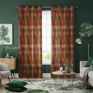 May include: A pair of orange, red, and green patterned curtains with a geometric design. The curtains are hung on a window in a room with a green wall, a wooden table, and a green rug.