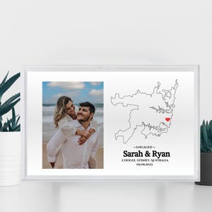 May include: Framed print with a photograph of a couple and a map of Sydney, Australia. The map has a red heart marking a location. Text reads "Engaged" and names "Sarah & Ryan" with a date.