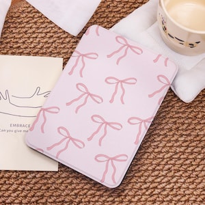 May include: A pink e-reader cover with a repeating pattern of pink bows. The cover is made of a soft, textured material.
