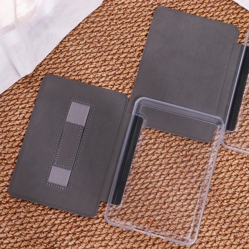 May include: A grey tablet case with a clear plastic frame. The case is open, showing a stand and a clear plastic holder. The case is on a textured brown surface.