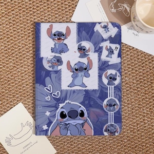 May include: A blue notebook featuring a collage of Stitch character illustrations. The cover has a floral pattern and multiple images of Stitch in various poses. The notebook is on a brown surface with a card that says "EMBRACE Can you give me a hug?"