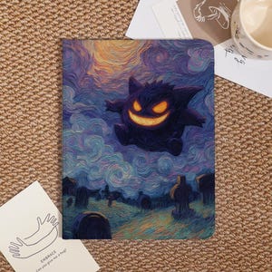 Peut inclure: Un carnet avec une illustration stylisée de Gengar dans un cimetière. L'œuvre d'art a un style pictural avec des nuages tourbillonnants et un sourire orange vif. Le carnet est rectangulaire et a une couverture souple.