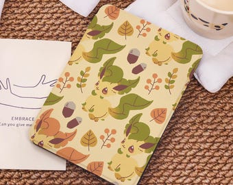 May include: A beige tablet case featuring a repeating pattern of cartoon-style creatures, leaves, and acorns in shades of green, brown, and orange. The case has rounded corners and a black border. The text "EMBRACE Can you give me" is visible on a card.