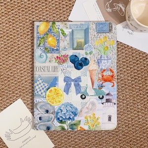 May include: A decorative notebook with a coastal theme. The cover features a collage of illustrations including lemons, blueberries, a crab, a lighthouse, and the text "Coastal Life". The color palette includes blue, yellow, and white.