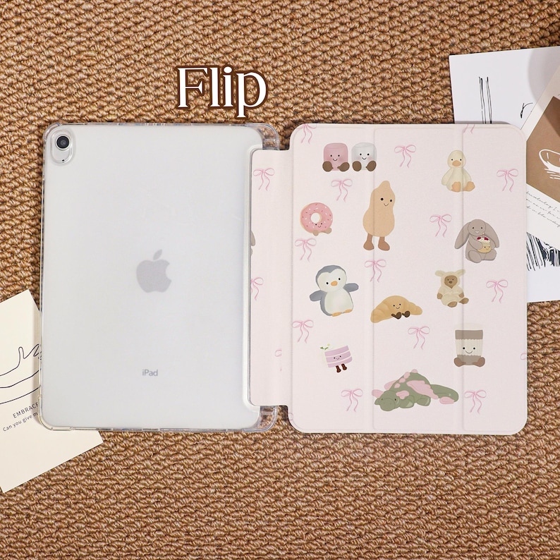 May include: A clear iPad case with a flip cover. The flip cover is light pink and decorated with cartoon illustrations of animals and food. The word "Flip" is printed in gold at the top of the image.