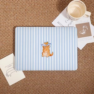 May include: A laptop sleeve with a light blue and white striped pattern. The sleeve features a watercolor illustration of an orange cat holding two fish. The background is a light blue and white striped pattern.