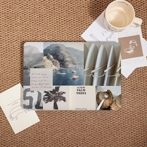 May include: A rectangular decorative tray with a collage of images, including a coastal scene, surfboards, and a palm tree. Text on the tray reads "A Few Palm Trees" and "Edward Roscha". A white mug and cards are on a woven surface.