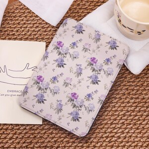 May include: A white e-reader cover with a floral pattern featuring purple and blue flowers on a white background.