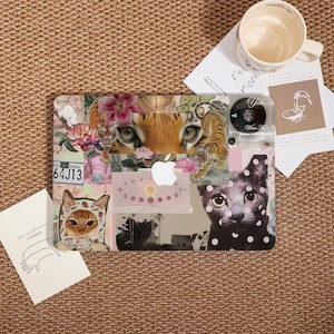 May include: A laptop case with a collage design featuring tiger eyes, flowers, and cat illustrations. The case includes a New York license plate graphic and a white Apple logo. A coffee mug and cards are next to the case.