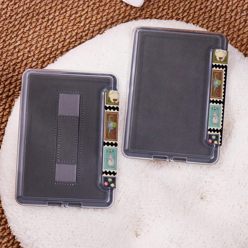 May include: Two clear plastic e-reader cases with a dark grey interior. Each case has a decorative strip with colourful postage stamp designs. One case has a built-in stand.