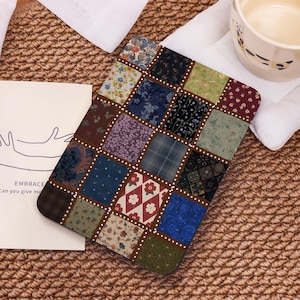 May include: A patchwork tablet case with a variety of floral and patterned fabric squares in shades of blue, green, red, and brown. The case has a brown border with white dotted accents. A white card with the word "EMBRACE" is visible.