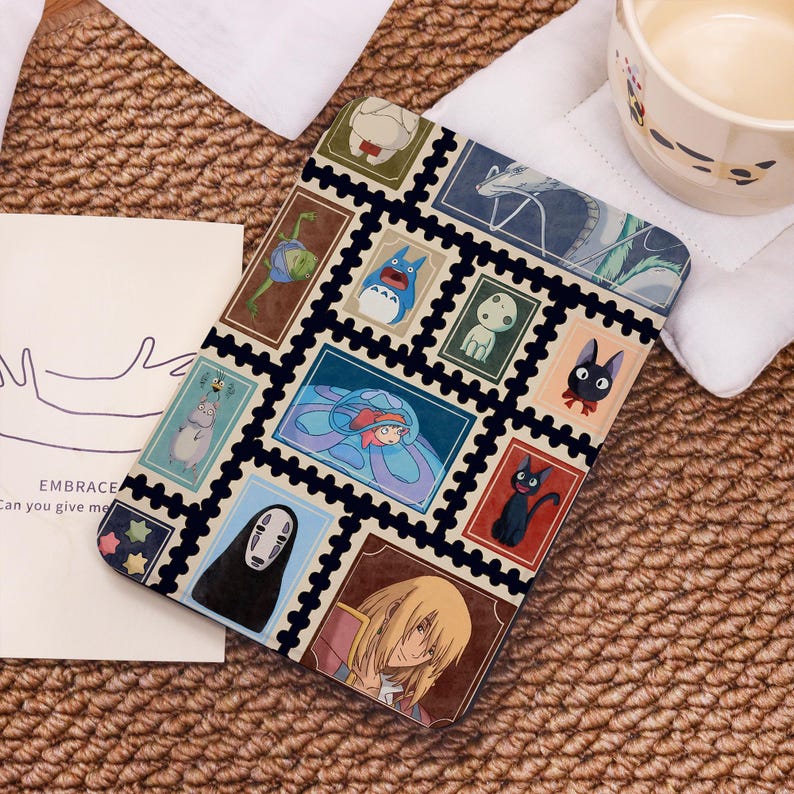 May include: A black tablet case with a collage of colourful anime-style illustrations resembling postage stamps. The case has a black border and a beige background. The text "EMBRACE Can you give me" is visible on a card.