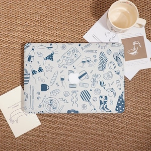 May include: A laptop case with a light blue background and a pattern of blue line drawings of beach and food-related items. The case has a white Apple logo in the center. A white mug and cards are on the side.