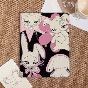 Könnte beinhalten: Eine schwarze und rosa Tablet-Hülle mit Illustrationen von Cartoon-Hasen. Die Hasen haben Schleifen, Sterne und Herzen, vor einem Hintergrund aus rosa Formen. Die Hülle hat eine weiche, matte Oberfläche.