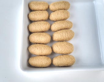 May include: A white ceramic square dish filled with twelve beige, oblong, textured objects. The objects are arranged in three rows of four. The objects have a fibrous appearance, and the dish is set against a white background.