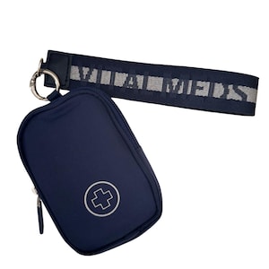 May include: A navy blue zippered pouch featuring a white medical cross symbol on the front. The pouch is attached to a matching navy blue wrist strap with the text VITAL MEDS woven in light gray lettering, connected by a silver metal ring.