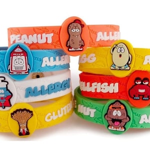 Può includere: Un set di otto braccialetti per allergie in silicone colorati con personaggi dei cartoni animati e testo. I braccialetti sono etichettati con allergeni comuni, tra cui arachidi, latticini, uova, crostacei, noci e glutine. I braccialetti sono un modo divertente e facile per far sapere agli altri delle tue allergie.