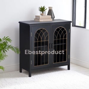 May include: Black cabinet with two doors and arched glass panels. The cabinet has a gold trim and sits on a white rug.