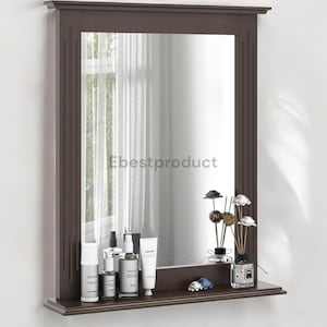 May include: A brown framed wall mirror with a shelf underneath. The shelf has several bottles of toiletries and a decorative vase with dried flowers.