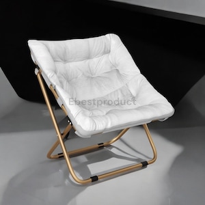 May include: A white, padded folding chair with a gold-colored metal frame. The seat and backrest are made of a soft, quilted material. The chair is designed for comfort and portability, suitable for indoor or outdoor use.
