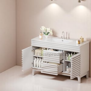 May include: White bathroom vanity with a white countertop and a white porcelain sink. The vanity has two drawers and a cabinet with a slatted door. The vanity is filled with toiletries and towels.