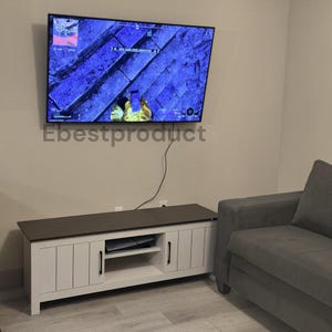 May include: A rectangular white media console with a dark brown top surface, two vertical-slatted cabinet doors featuring black handles, and an open center shelf. A flat-screen television is mounted on the wall above the console.
