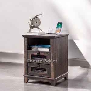 May include: A rustic, dark-stained wooden nightstand with two drawers and a shelf. The top surface holds a decorative clock, a charging station, and a smartphone. The drawers have metal mesh inserts and black hardware. The nightstand is designed for bedroom use.