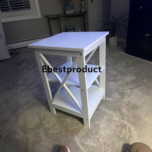May include: A white square side table featuring a flat top surface, two lower shelves, and an X-shaped support frame on the sides. The text Ebestproduct is printed in black on the middle shelf area of the furniture piece.