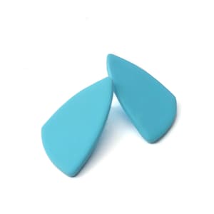 May include: Two light blue, teardrop-shaped earrings. The earrings have a smooth, matte finish and are set against a white background. The earrings are a solid color and have a simple, modern design.