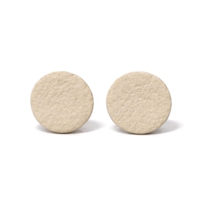 May include: Two beige, circular earrings with a textured surface. The earrings are set against a white background, highlighting their simple, minimalist design. The earrings are likely made of a soft material.