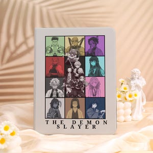 May include: A white tablet case with a grid of anime character portraits in various colours. The case has the text "THE DEMON SLAYER" at the bottom. The portraits are in shades of green, purple, red, and blue.