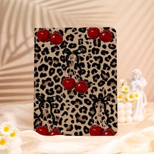 May include: A rectangular case featuring a leopard print background with red cherries and black bows. The cherries are clustered in groups of two or three, adding a playful contrast to the animal print.