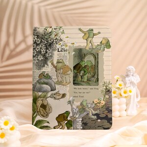 Könnte beinhalten: Eine rechteckige Tablethülle mit einer Collage aus Vintage-Illustrationen von Fröschen und Kröten, Blumenmotiven und Zeitungsausschnitten. Der Text lautet: "We look brave," said Frog. "Yes, but are we?" asked Toad. Das Design verwendet gedämpfte Grün- und Beigetöne.