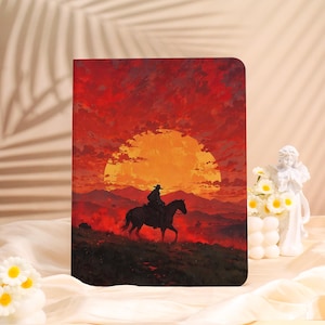 Könnte beinhalten: Ein Notizbuch mit einer Illustration zum Thema Western. Das Cover zeigt einen Cowboy auf einem Pferd, der sich vor einem Sonnenuntergang in Orange- und Rottönen abhebt. Das Notizbuch ist rechteckig und scheint aus Papier zu sein.