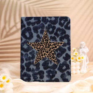 May include: A blue journal with a leopard print pattern and a large star in the center. The star has a tan and black leopard print design. The journal is sitting on a cream-colored surface.