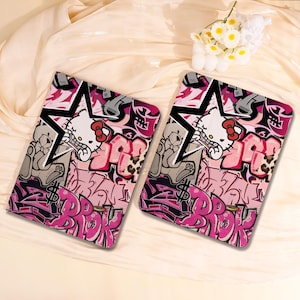 May include: Two rectangular cases with a graffiti-style design. The cases feature a pink, black, and grey colour scheme with a cartoon cat character, stars, and the word "BROK" in pink graffiti lettering.